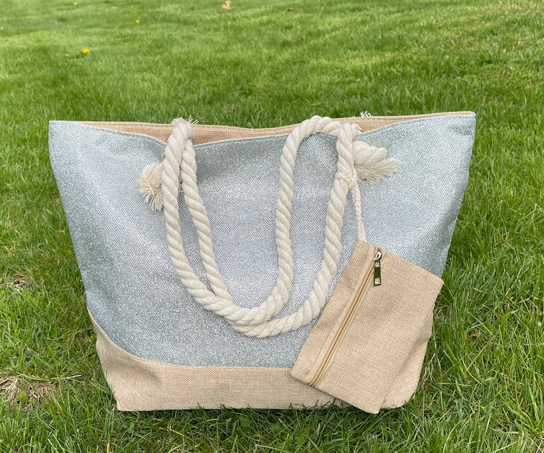 May include: A silver glitter tote bag with a natural canvas bottom and rope handles. The bag has a small zippered pouch attached to the front.
