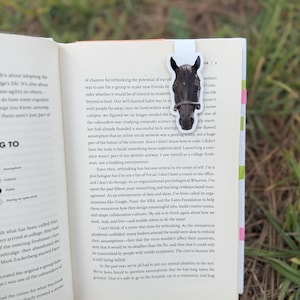 May include: A bookmark featuring a horse head design. The horse is dark brown with a white background. The bookmark is inserted into a book with text visible.