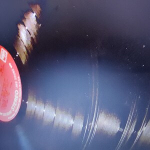 May include: A red vinyl record with a Columbia Records label. The record is black and has visible grooves. The label has the words "Columbia" and "Stereo" printed on it.