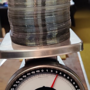 May include: A silver postal scale with a black face and a red needle. The scale reads 4.3 pounds. The scale is made in China. The scale is labeled "pelouze" and "Model Y50".