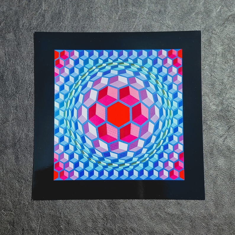 May include: A framed print of an optical illusion artwork featuring a blue, pink, and red geometric pattern. The pattern creates the illusion of a sphere.