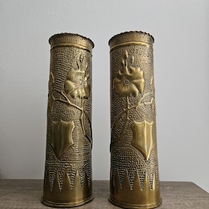 May include: A pair of gold-toned metal vases with embossed floral designs. The vases are cylindrical in shape and have a textured surface.