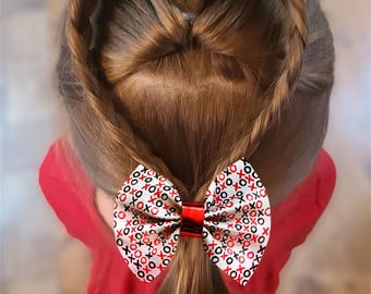 Puede incluir: Una niña con cabello castaño peinado en forma de corazón con un lazo blanco y rojo con el texto "XOXO" repetido en él.