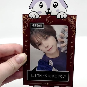 May include: A rectangular photo holder featuring a cartoon light purple wolf at the top and bottom. The frame is dark red with gold filigree, the text &TEAM, and a speech bubble at the bottom that reads I... I THINK I LIKE YOU!
