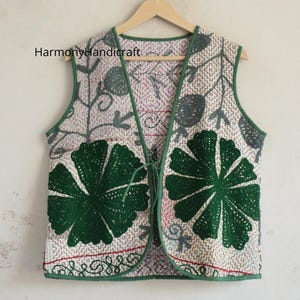 May include: A sleeveless waistcoat featuring a light-coloured base with a kantha-style stitched pattern, accented by large dark green floral appliqués on the front panels. The garment includes green trim, a tie closure, and the text HarmonyHandicraft.