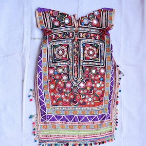 Può includere: Una tunica ricamata con intricati specchi e motivi geometrici. L'indumento presenta una vibrante tavolozza di colori rosso, viola, verde e arancione, con nappe decorative lungo i bordi. Probabilmente si tratta di un capo tradizionale o etnico.