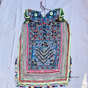 May include: A vibrantly embroidered textile with a central blue panel featuring a tree design. The piece is adorned with colorful geometric patterns, red, green, and yellow accents, and a fringe of tassels along the bottom. The textile is likely a decorative item.