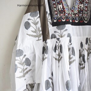 Puede incluir: Vestido t&uacute;nica blanco con cuello en V y estampado floral. El vestido presenta un canes&uacute; y mangas marrones, y el escote est&aacute; adornado con bordados coloridos. Las mangas tienen un estampado floral. El texto "Harmony Handicraft" es visible.