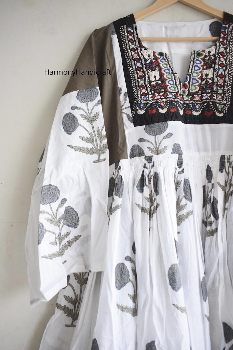 Puede incluir: Vestido t&uacute;nica blanco con cuello en V y estampado floral. El vestido presenta un canes&uacute; y mangas marrones, y el escote est&aacute; adornado con bordados coloridos. Las mangas tienen un estampado floral. El texto "Harmony Handicraft" es visible.