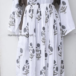 Puede incluir: Un vestido largo blanco con estampado floral y mangas largas. El vestido presenta un canes&uacute; marr&oacute;n con detalles bordados y el texto "HarmonyHandicraft". El vestido se exhibe en un maniqu&iacute;.