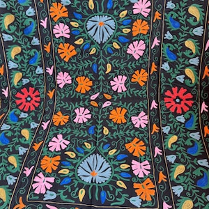 May include: Black textile with colorful floral embroidery. The design features a central floral motif with blue, pink, orange, and red flowers, surrounded by green leaves and vines. The border has a repeating paisley pattern.
