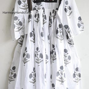 Puede incluir: Vestido de algod&oacute;n blanco con estampado floral gris. El vestido presenta un escote bordado y paneles de hombro marrones. Las mangas son de tres cuartos. El texto "HarmonyHandicraft" es visible en el lado izquierdo del vestido.