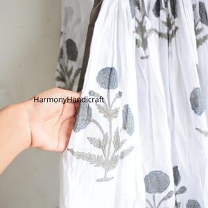 Puede incluir: Tela blanca con un estampado floral en gris y azul. La tela forma parte de una prenda, posiblemente un vestido o una falda, con cintura fruncida. El texto "HarmonyHandicraft" es visible en la tela.