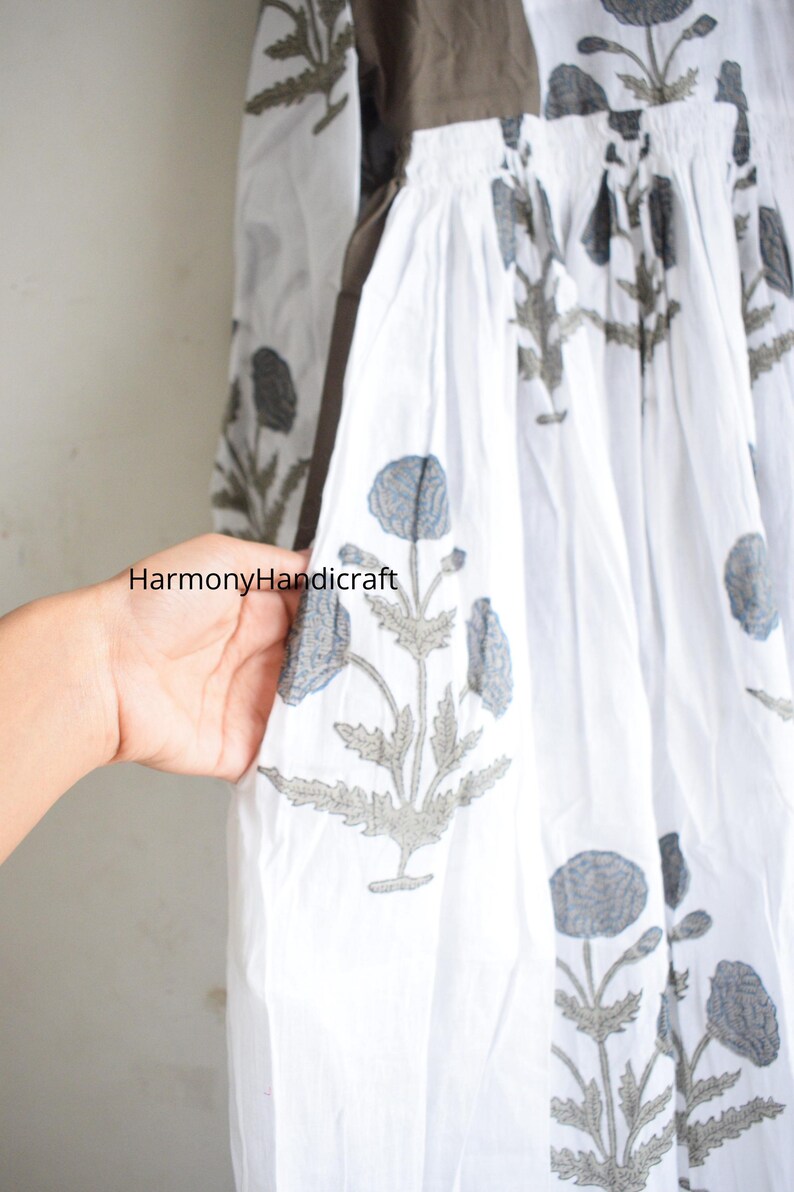 Puede incluir: Tela blanca con un estampado floral en gris y azul. La tela forma parte de una prenda, posiblemente un vestido o una falda, con cintura fruncida. El texto "HarmonyHandicraft" es visible en la tela.