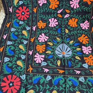 May include: Black textile with colorful floral embroidery. The design features red, orange, pink, blue, and yellow flowers and paisley shapes, with green vines and gold accents. The embroidery is detailed and covers the entire surface.
