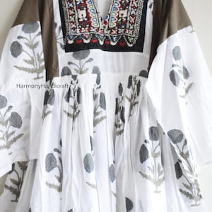 Puede incluir: Vestido blanco con estampado floral gris y escote bordado. El vestido presenta mangas largas con paneles de hombros marrones y un escote en V. El texto "HarmonyHandicraft" es visible.