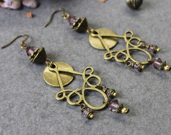 May include: A pair of dangle earrings featuring antique brass-toned metal filigree components, circular discs, and faceted light purple crystal beads. Each earring is suspended from a curved metal hook and includes decorative metal bead caps.