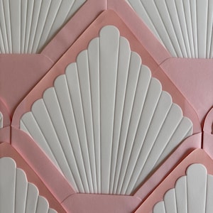 May include: Close-up of a pattern of white paper with a fan-like design, set within pink paper envelopes. The envelopes are arranged in a repeating geometric pattern, creating a visually appealing texture. The image is well-lit, highlighting the details.