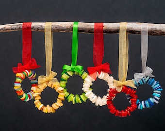 May include: Six colorful button wreaths hanging from a branch. The wreaths are made of various colors of buttons, including red, yellow, green, blue, and white. The wreaths are tied with ribbon and are ready to be hung on a Christmas tree or used as a festive decoration.
