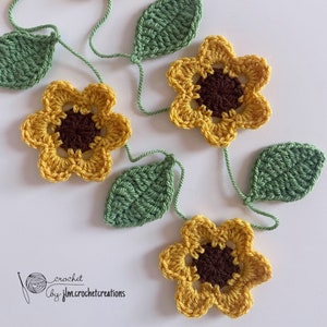 Peut inclure: Une guirlande de tournesols en crochet avec des fleurs jaunes et des feuilles vertes. La guirlande est enfilée avec un fil vert fin. Le texte "crochet by jlm.crochetcreations" est visible dans le coin inférieur gauche de l'image.