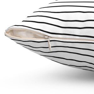 May include: A white pillow with black horizontal stripes and a zipper closure.