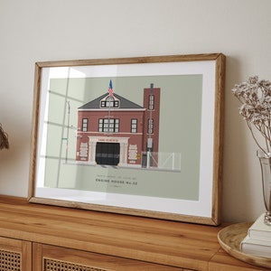 May include: A framed illustration of a red brick firehouse with a white door and a sign that reads "Engine House No. 32". The firehouse has a green roof and a small American flag on top. The illustration is on a light green background.