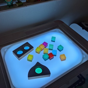 May include: A light-up table with a variety of colorful translucent blocks and wooden shapes. The table has a blue light that shines through the blocks, creating a colorful display.