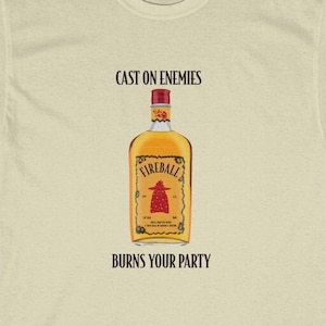 May include: A beige t-shirt featuring the text "Cast on enemies" and a Fireball whiskey bottle graphic. The text "Burns your party" is positioned below the graphic.