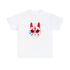 以下が含まれることがあります： 白いTシャツに、赤と白の狐のマスクが描かれています。マスクの左側に青い涙が描かれています。