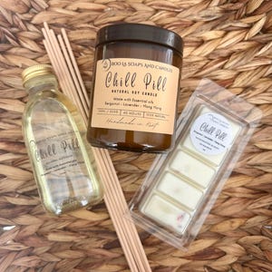 Könnte beinhalten: Eine Auswahl an Aromatherapie-Produkten, darunter eine braune Glas-Kerze, eine klare Glasflasche und Wachsschmelzen, alle mit dem Label "Chill Pill". Die Kerze und die Wachsschmelzen sind mit Bergamotte, Lavendel und Ylang-Ylang beduftet. Auf einer gewebten Oberfläche.