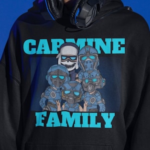 Puede incluir: Una sudadera con capucha negra con un estampado gráfico azul de un grupo de personajes de dibujos animados con cascos y el texto "CARMINE FAMILY".