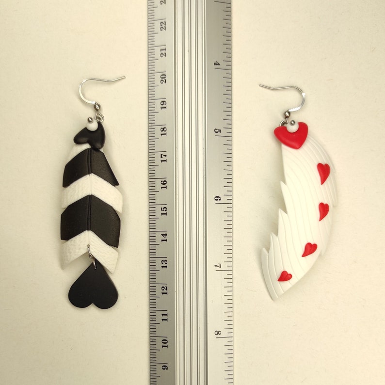 May include: A pair of handmade polymer clay earrings. One earring is black and white with a chevron pattern and a black heart. The other earring is white with red hearts and a jagged edge.