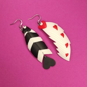 May include: A pair of dangle earrings with a black and white feather design on one earring and a white feather with red hearts on the other earring.