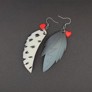 May include: A pair of dangle earrings featuring a black and white feather design and a solid black feather design. Each earring has a red heart charm.