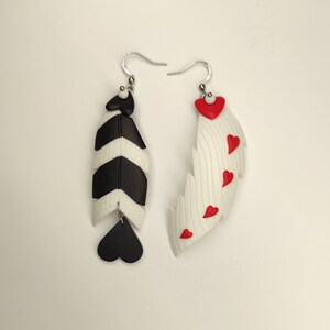 May include: A pair of dangle earrings with a black and white striped feather design on one earring and a white feather with red hearts on the other earring.