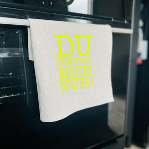 Könnte beinhalten: Ein helles Küchentuch mit den Worten "DU BENUTZT MICH NUR!" in leuchtendem Gelb. Das Tuch hängt an einer schwarzen Backofentür. Der Ofen hat eine Digitaluhr, die 08:30 anzeigt.