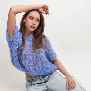 May include: A woman wearing a light blue, loose-fitting, knit sweater with a subtle striped pattern. The sweater has short sleeves and a relaxed fit.