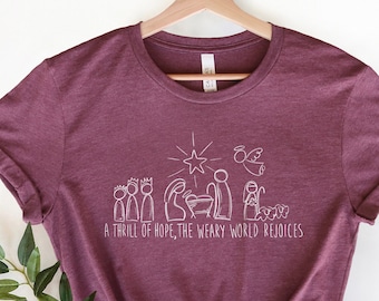 May include: A maroon t-shirt with a white design of the nativity scene and the text "A thrill of hope, the weary world rejoices".