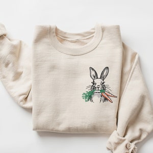 May include: A beige sweatshirt with a graphic of a rabbit eating carrots.