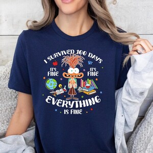 K&ouml;nnte beinhalten: Ein marineblaues T-Shirt mit einer Comicfigur und dem Text "Ich habe 100 Tage &uuml;berlebt. Es ist in Ordnung. Alles ist in Ordnung."