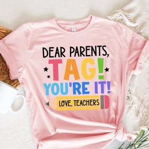 May include: Pink t-shirt with the text "Dear Parents, *TAG!* You're It! Love, Teachers" and a rainbow colored pencil graphic.