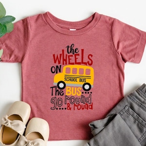 May include: A red toddler t-shirt with the text "The wheels on the school bus go round and round" and a yellow school bus graphic.
