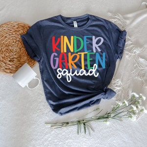 May include: A dark blue t-shirt with the text "kindergarten squad" in rainbow colors.