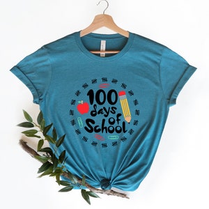 May include: A teal blue t-shirt with a graphic design that says "100 days of school" with a red apple, a yellow pencil, and paper clips.