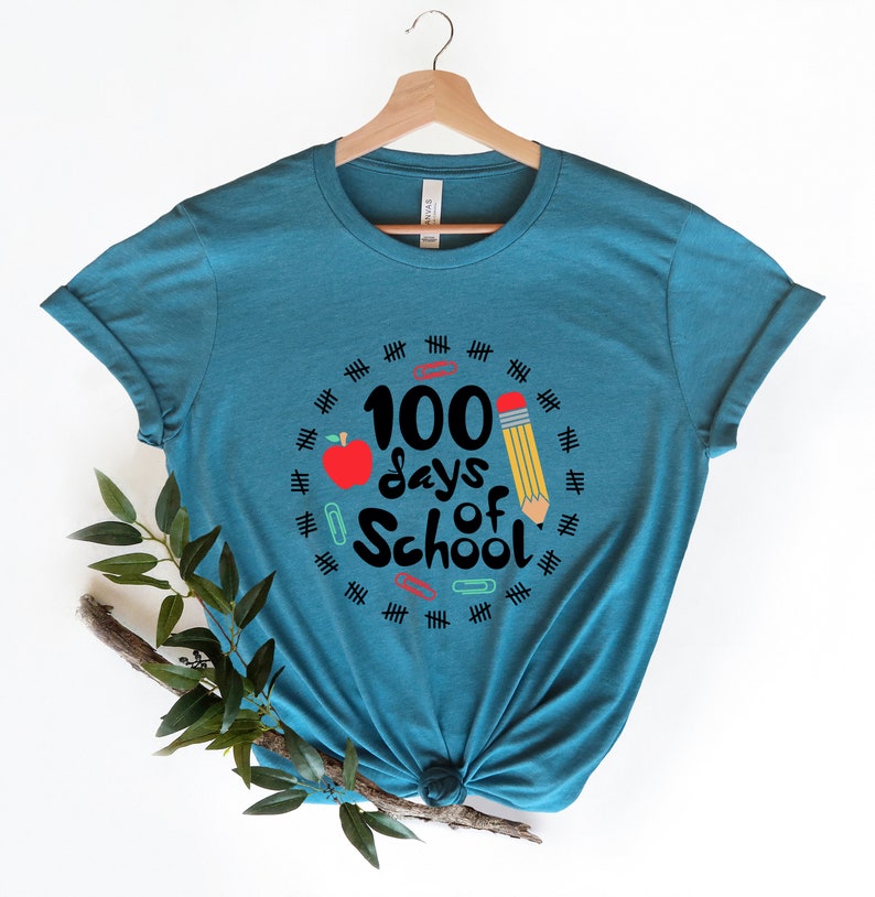 May include: A teal blue t-shirt with a graphic design that says "100 days of school" with a red apple, a yellow pencil, and paper clips.