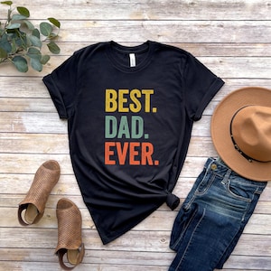 May include: Black t-shirt with the text "BEST. DAD. EVER." in a vintage style font with yellow, green, and orange colors.