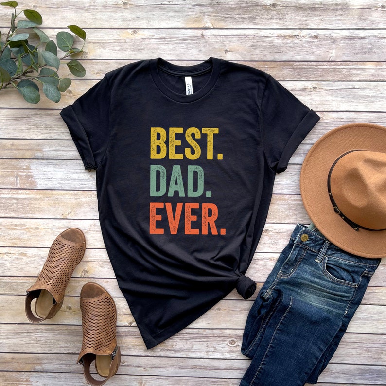 May include: Black t-shirt with the text "BEST. DAD. EVER." in a vintage style font with yellow, green, and orange colors.