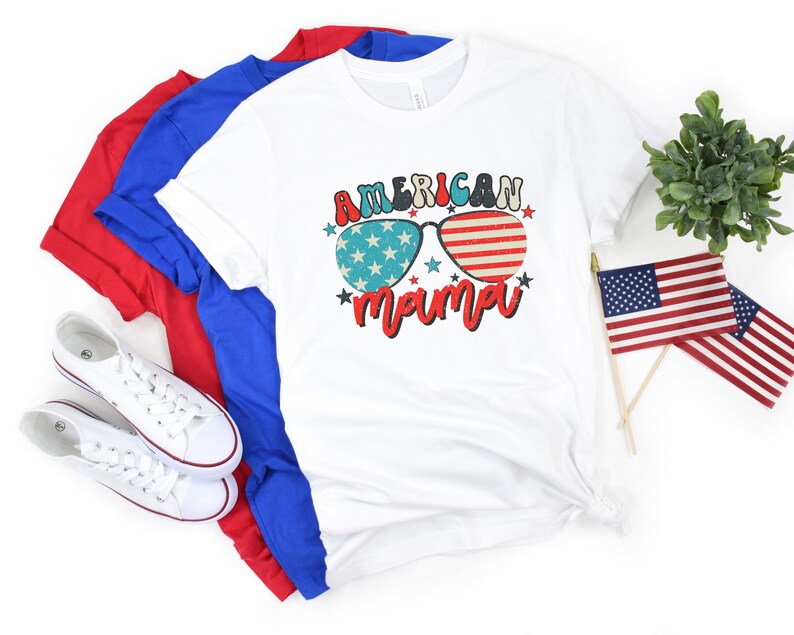 Puede incluir: Camiseta blanca con un gr&aacute;fico de gafas de sol rojo, blanco y azul con el texto "American mama" debajo.
