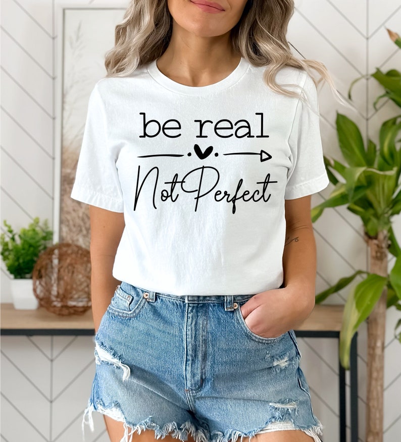 May include: White t-shirt with black text that reads "be real - not perfect" with a heart and arrow graphic.