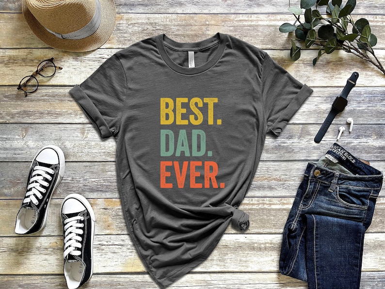 May include: A dark gray t-shirt with the text "BEST. DAD. EVER." in a vintage style font. The text is in yellow, green, and orange.